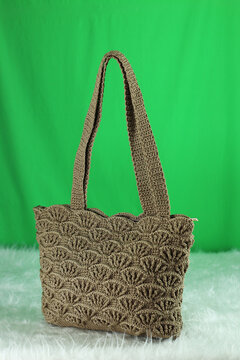 Crocheted  beige bag on a white fluffy blanket in front of a green background.