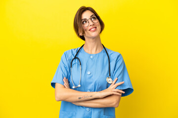 Surgeon doctor woman isolated on yellow background looking up while smiling