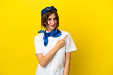 Airplane stewardess woman isolated on yellow background pointing to the side to present a product