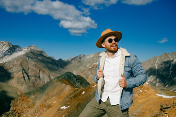 Young caucasian male in hat and sunglasses adventurer posing in mountainous landscape