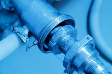 Metal plumbing pipes with connectors and water droplets in close-up view in milk factory