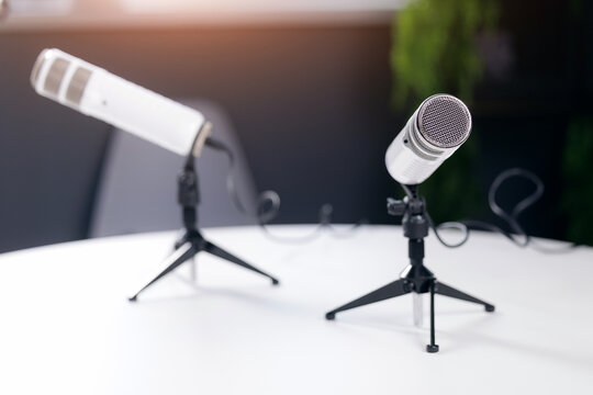 Two white microphones on stands in podcast studio setting