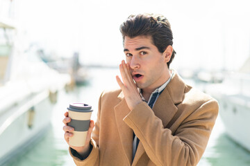 Young handsome man holding a take away coffee at outdoors whispering something