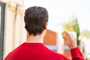Young handsome man holding a Bitcoin at outdoors in back position