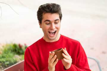 Young handsome man holding a wallet with surprised expression