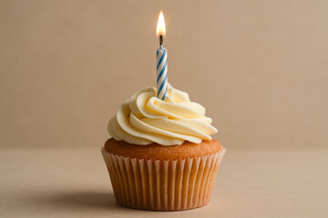 Single vanilla birthday cupcake with blue striped candle and buttercream frosting on beige background. Minimalist celebration concept with copy space.
