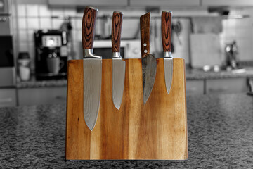 Japanese knife set on a wooden board. In the background, blurred in black and white, the kitchen.