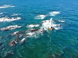 Aerial view of offshore lighthouse on rocky reef in clear blue ocean