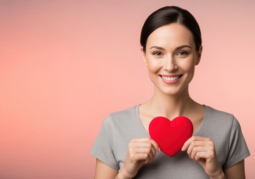 Beautiful smiling woman holding a red heart shape expressing love and care