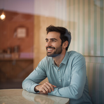 A smiling man sitting by a table under gentle shop lighting, soft pastel background and subtle reflection on surface, shallow depth at f/2.5, low ISO ensuring clean tones, white balance