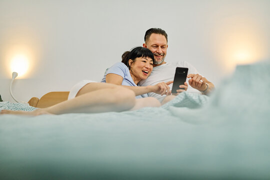 Portrait of a lovely young couple or friends having fun together using a mobile phone in bed at home