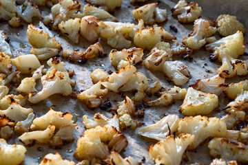 Pieces of baked cauliflower in baking tray on wooden table