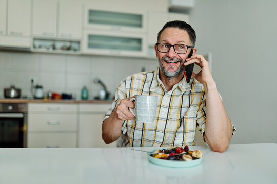 Man enjoying breakfast while using smartphone in modern kitchen during morning hours