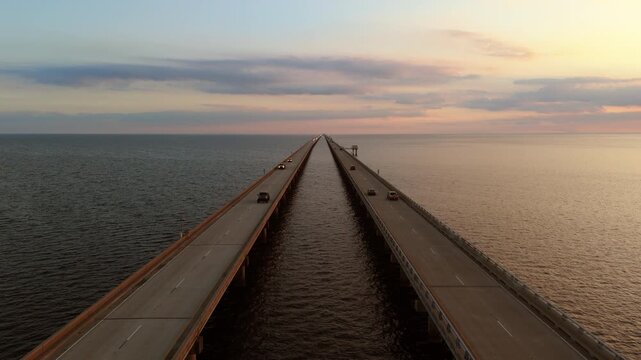 A slow-motion drone shot flying between the northbound and southbound spans of the Causeway Bridge, facing south over Lake Pontchartrain during golden hour.