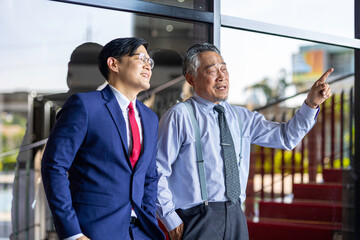 Two businessmen of different generations in formal suits networking and discussing ideas outside an office, representing workplace mentorship, collaboration, and professional growth.