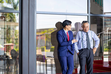 Two businessmen of different generations in formal suits networking and discussing ideas outside an office, representing workplace mentorship, collaboration, and professional growth.