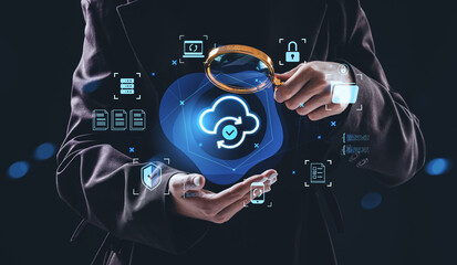 Businessman holding magnifying glass over cloud sync icon with data security symbols, representing...