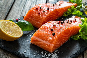 Fresh raw salmon steaks on black stony board on wooden background