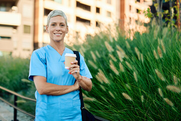 Nurse in scrubs enjoying coffee outside a modern medical facility during a sunny day