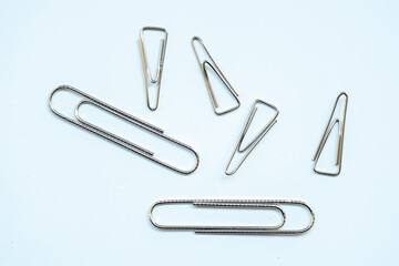 A scatter of six silver paper clips on a light blue-white background. The group consists of two...