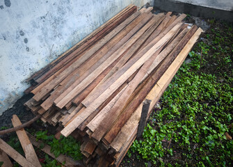 Fototapeta premium Stack of wooden planks outdoors against old wall, raw lumber materials for construction and carpentry work