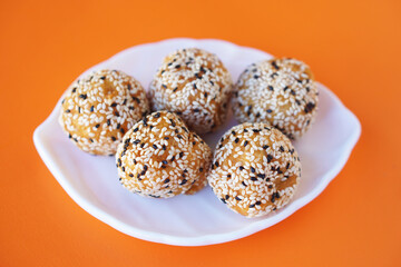 Golden Thai “Khanom Khai Hong” sesame balls on white plate, mix of white and black sesame seeds on round fried flour. Concept, homemade Thai traditional dessert, snack. Selective focus on the front. 