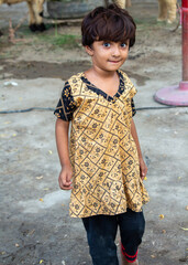 Smiling Child in Traditional Printed Clothing Standing Outdoors in a Rural Village Setting
