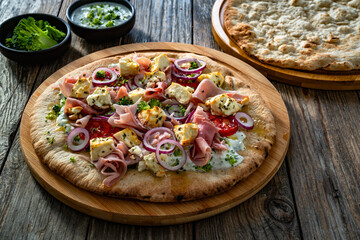 Pizza with boiled ham, feta cheese, tomatoes, red onion and broccoli dip on wooden table	