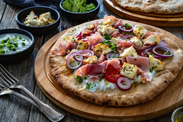 Pizza with boiled ham, feta cheese, tomatoes, red onion and broccoli dip on wooden table	