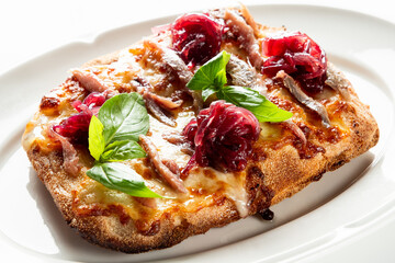 Gourmet rectangular flatbread pizza with melted cheese, anchovies, caramelized red onion, and fresh basil served on a white plate