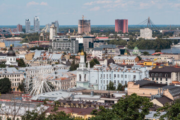 Fototapeta premium Panoramic view of Kyiv historic Podil district with ferris wheel and Dnipro River Panoramic cityscape of Kyiv, Ukraine, showing the historic Podil district with its white ferris wheel, old churches an