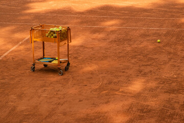 Fototapeta premium Coaching cart filled with tennis balls and rackets placed on clay court, emphasizing structured learning and sports preparation