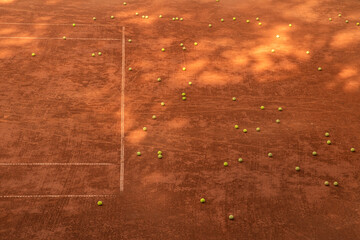Multiple tennis balls lie across an empty clay court, reflecting practice intensity and structured sports preparation