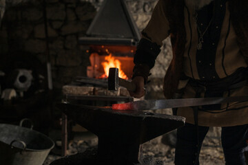 A Viking blacksmith with a white beard and braided hair works intently at a forge, hammering glowing metal on an anvil, with flames flickering in the background of a stone workshop.