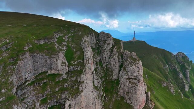 Grey dramatic cloudscape gathered above the mountains with steep cliffs. Drone footage distancing from the Cross at the Caraiman Peak in the Bucegi Mountains, Romania.
