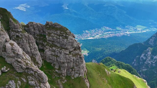 Approaching steep unapproachable rocks in the Bucegi Mountains, Romania. Revealing view on the residential area located in the green valley at the mountain foot.