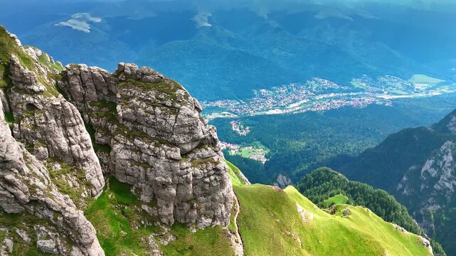 Steep rocks covered with green grass. Drone footage in the Bucegi Mountains, Romania. A beautiful town located in the valley among the mountains.