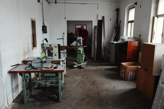 Man Clearing an Overfilled Workshop by Transporting a Large Heavy Industrial Machine Loaded on a Pallet Truck and Moving It Out of the Building as Part of a Complete Renovation and Cleanup Process