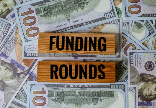 Funding Rounds: Wooden Blocks on a Background of One Hundred Dollar Bills Representing Startup Investment and Capital Raising - Powered by Adobe