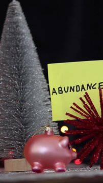 Varios adornos navide&ntilde;os y un cerdo de color rosado rodeados de luces de colores con una nota  de color amarillo con la palabra abundancia para la familia en el nuevo a&ntilde;o. Video Vertical