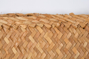 A close-up view of the rough, woven edge of a natural straw or reed mat texture, with a visible zigzag pattern, against a white background