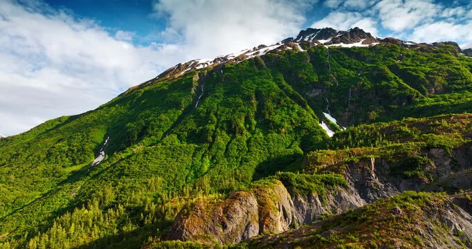 Green mountain slopes with summer snow. Bright green Alaskan slopes are streaked with thin summer snowfields under blue sky.