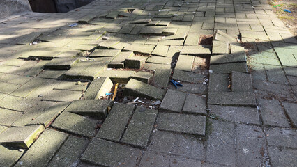Damaged sidewalk with uneven, broken paving stones and scattered debris creating a hazardous urban...