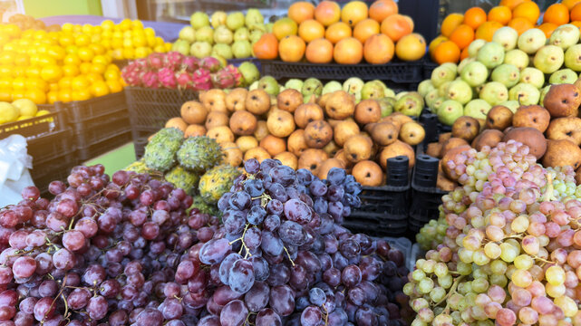 Abundant display of fresh grapes, pears and citrus fruits arranged in colorful piles at an outdoor market stand in bright daylight