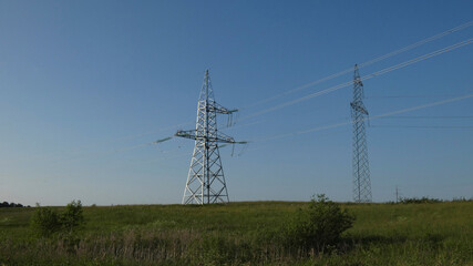 Two tall power transmission towers standing in a green field under a clear blue sky in the afternoon