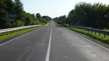 Long straight road surrounded by greenery on a sunny day in a rural area