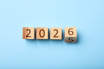 New year. Flipping cube with number 5 and 6 to make 2026 on light blue background, top view