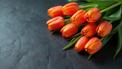 Orange tulips lie on dark textured table. Fresh flowers, green stems, elegant petals create bright, minimalist spring still life composition. Natural beauty.