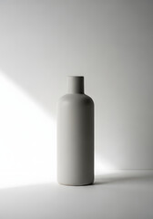 A minimalist gray bottle with a narrow neck stands against a white background with soft lighting.