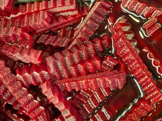 A detailed, overhead close-up of dark red beetroot cut into thick, crinkle-cut strips, submerged in its own deep red liquid/juice.